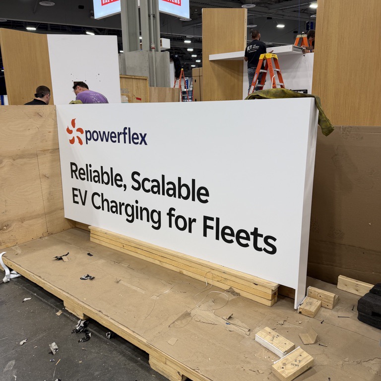 Real photo: a booth wall panel lettered with a logo and a two-line tagline in cut vinyl, while the booth was still being built (product photo 2 of 3)