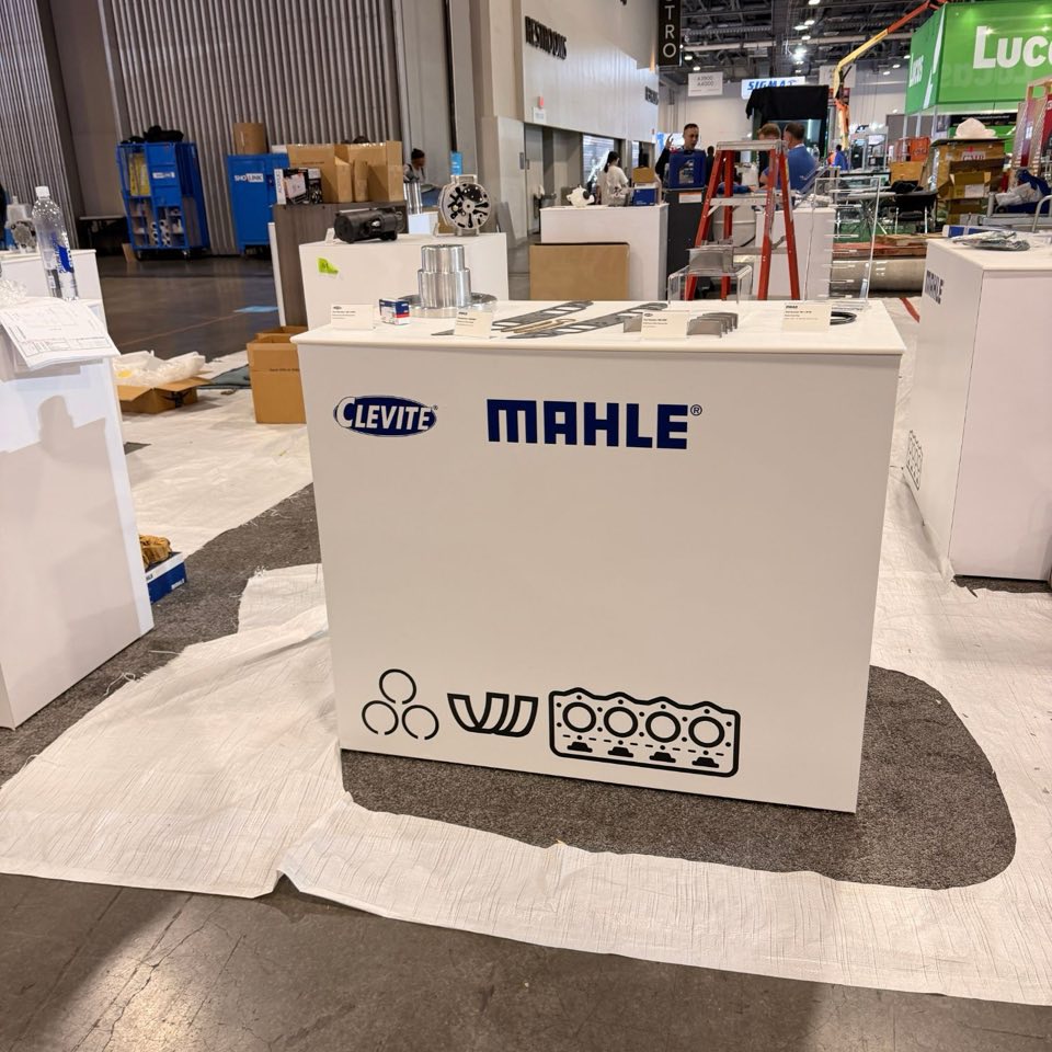 Real photo: a white exhibit counter with two brand logos and a row of part icons in solid-color cut vinyl, put up during show move-in